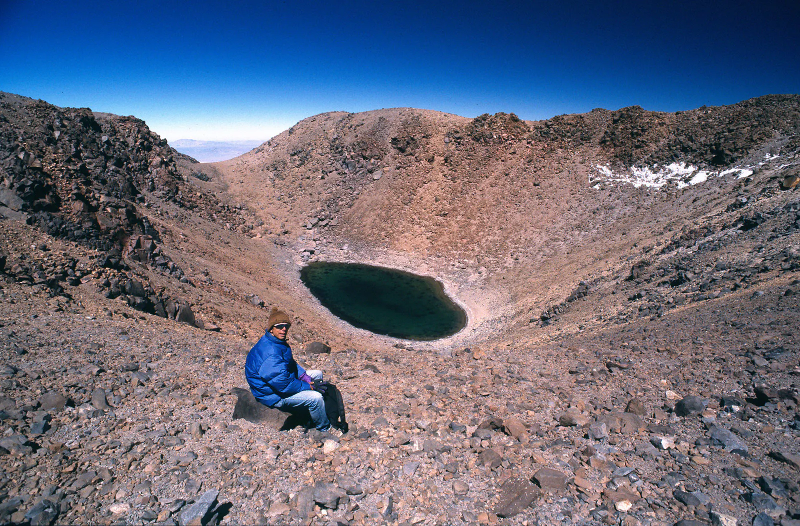 Hombre sentado frente a laguna en la cima de un volcán