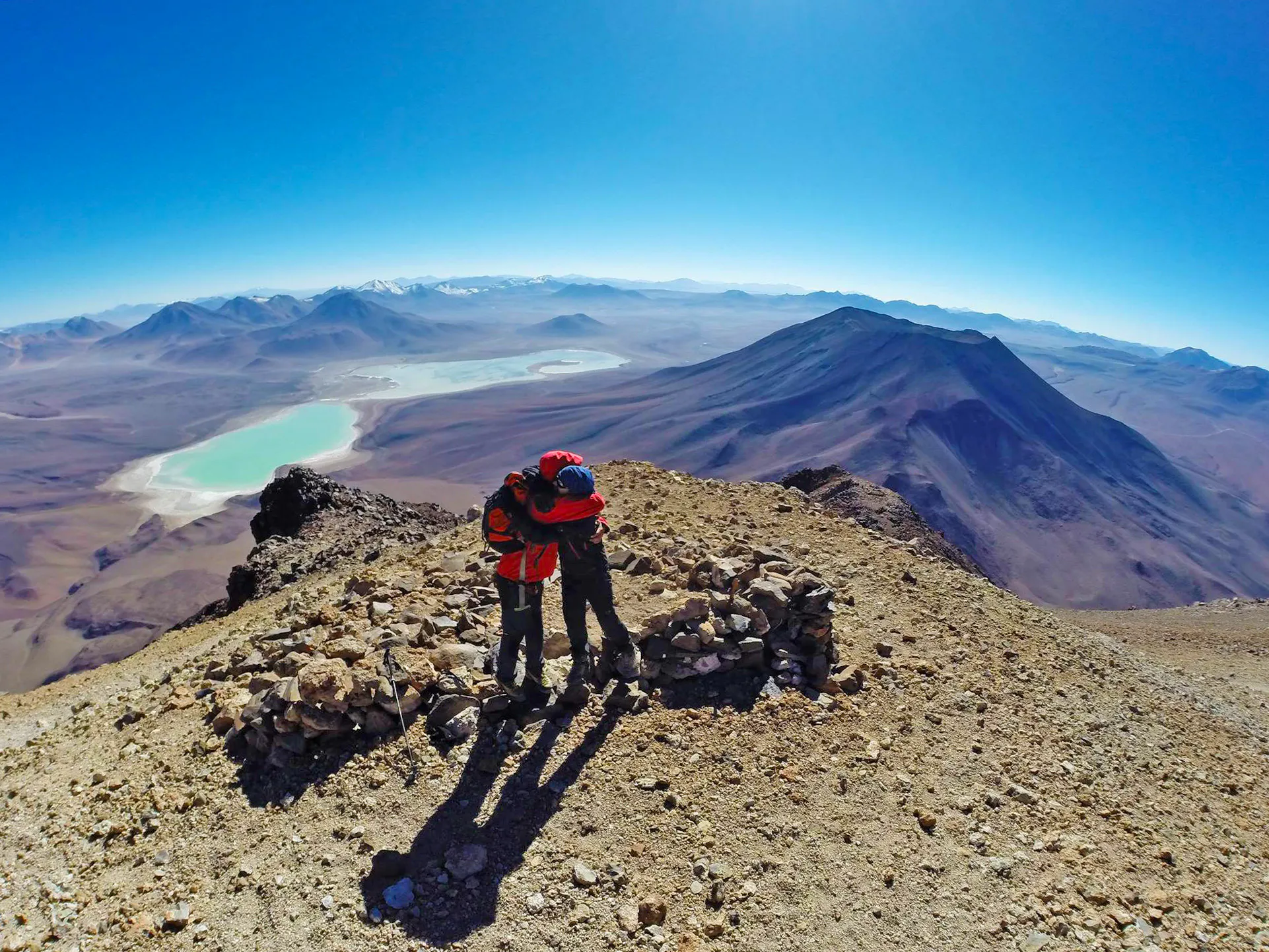 Dos escaladores se abrazan en cumbre con volcanes de fondo