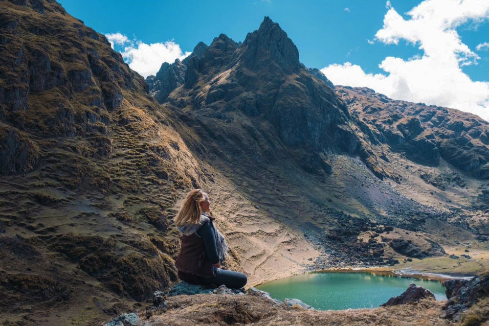 Mujer sentada frente a montaña y laguna esmeralda