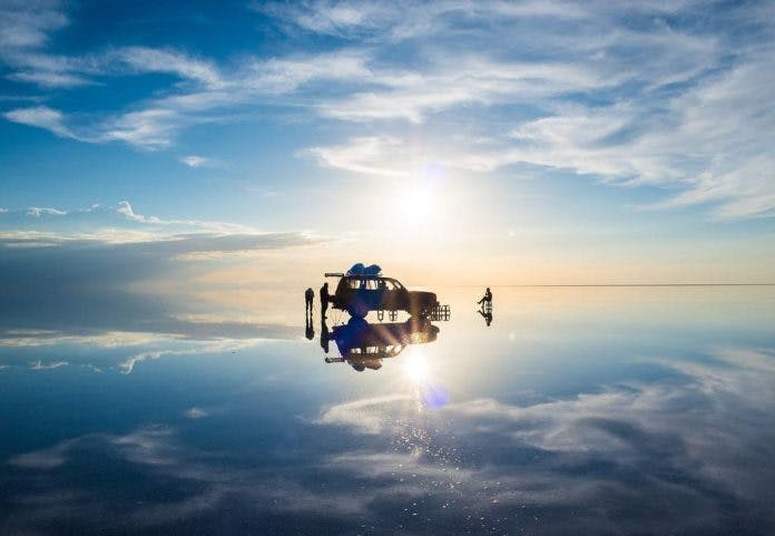 Automovil y viajeros sobre salar de uyuni durante efecto espejo