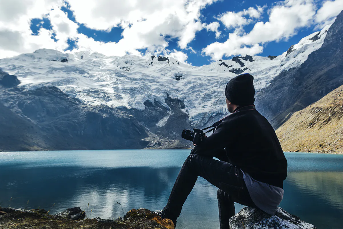 Viajero sentado frente a laguna y nevado