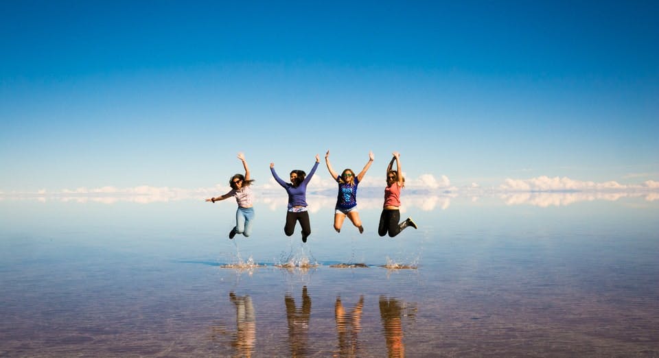 Jóvenes saltando en salar con efecto espejo