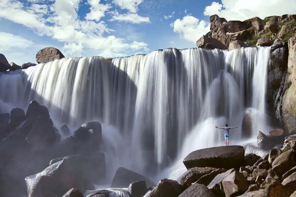 Catarata y hombre parado frente a ella