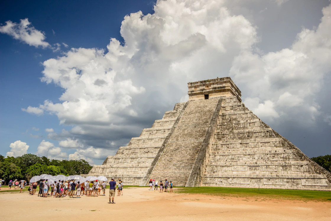 Grupo de viajeros bajo sombrilleros en CHichén Itzá