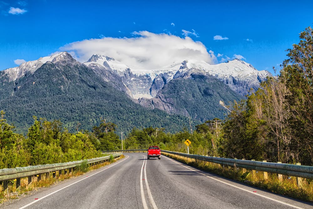 Auto rojo en carretera con montaña de fondo