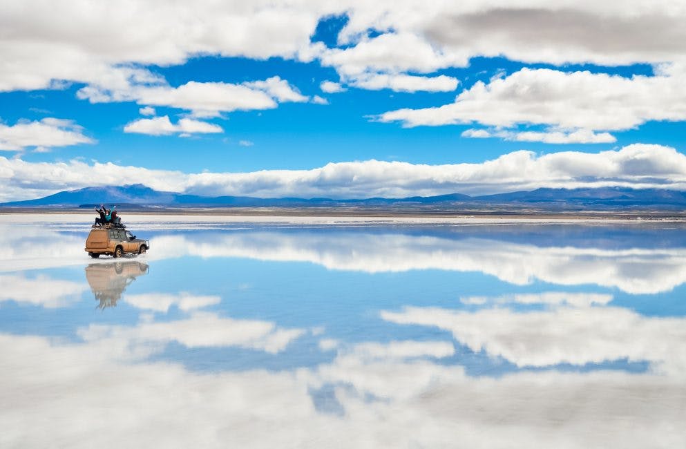 Auto enmedio de salar de uyuni inundado y reflejando el cielo