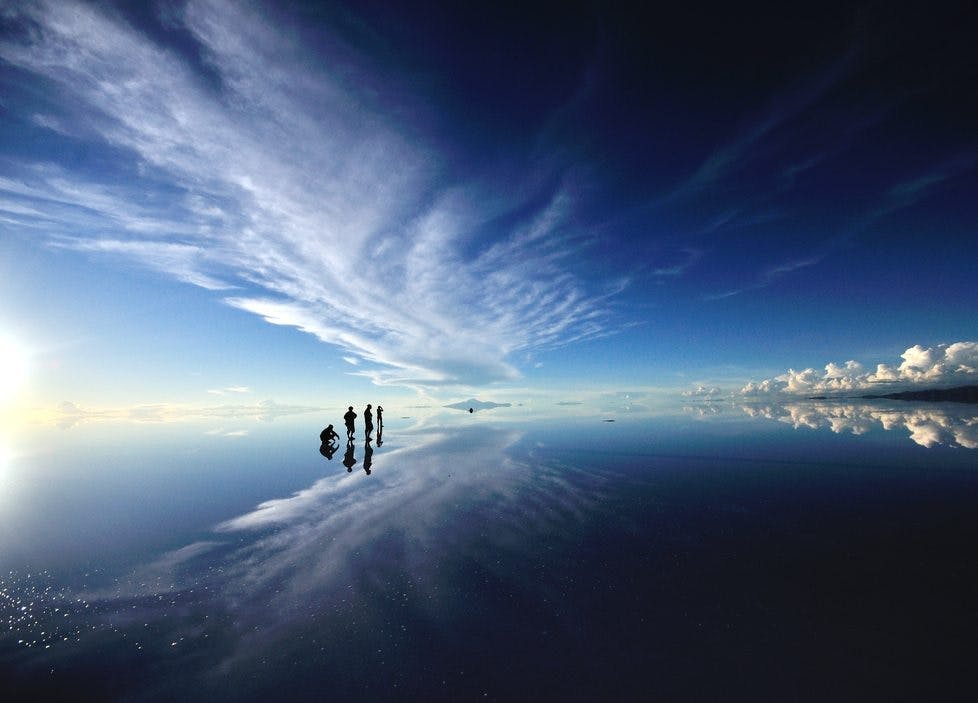 Viajeros parados en salar de uyuni durante efecto espejo